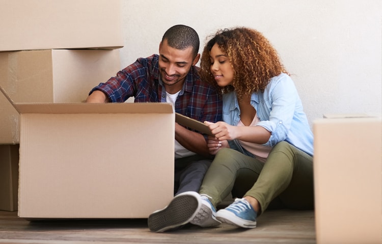 Couple sitting on the floor packing cardboard boxes to move 