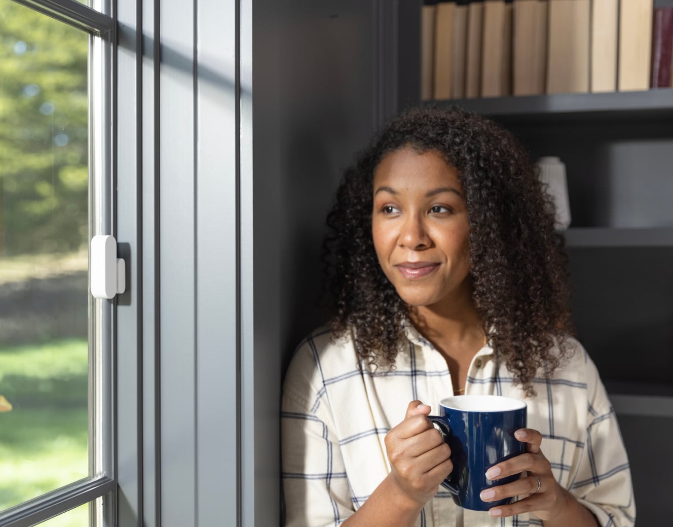 Woman drinking out of a mug and staring out the window with a window sensor