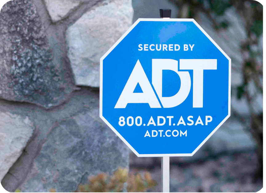 An ADT yard sign against a stone wall 