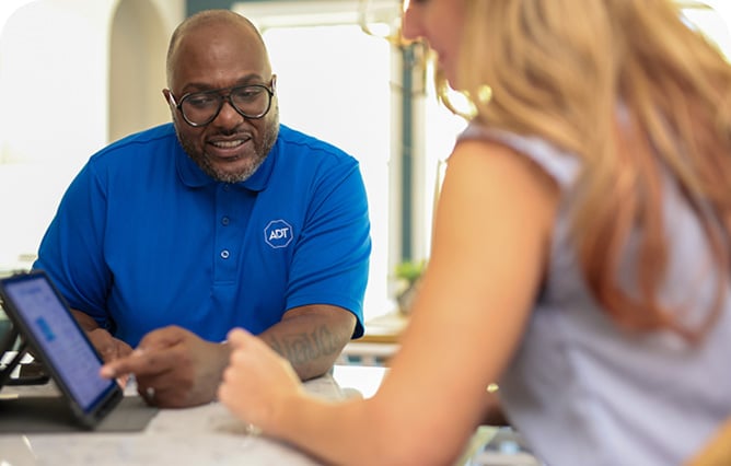 Woman self installing an ADT indoor camera on a shelf in her home Woman self installing an ADT indoor camera on a shelf in her home
