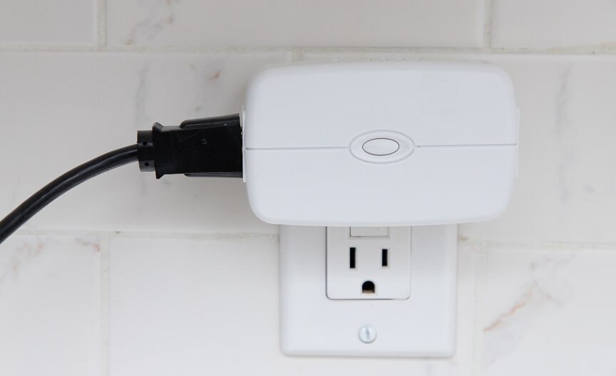 A portable ADT panic button device clipped onto the belt of a person wearing business-casual clothes. An ADT smart plug inserted into a wall outlet, providing remote control and energy management for connected devices.