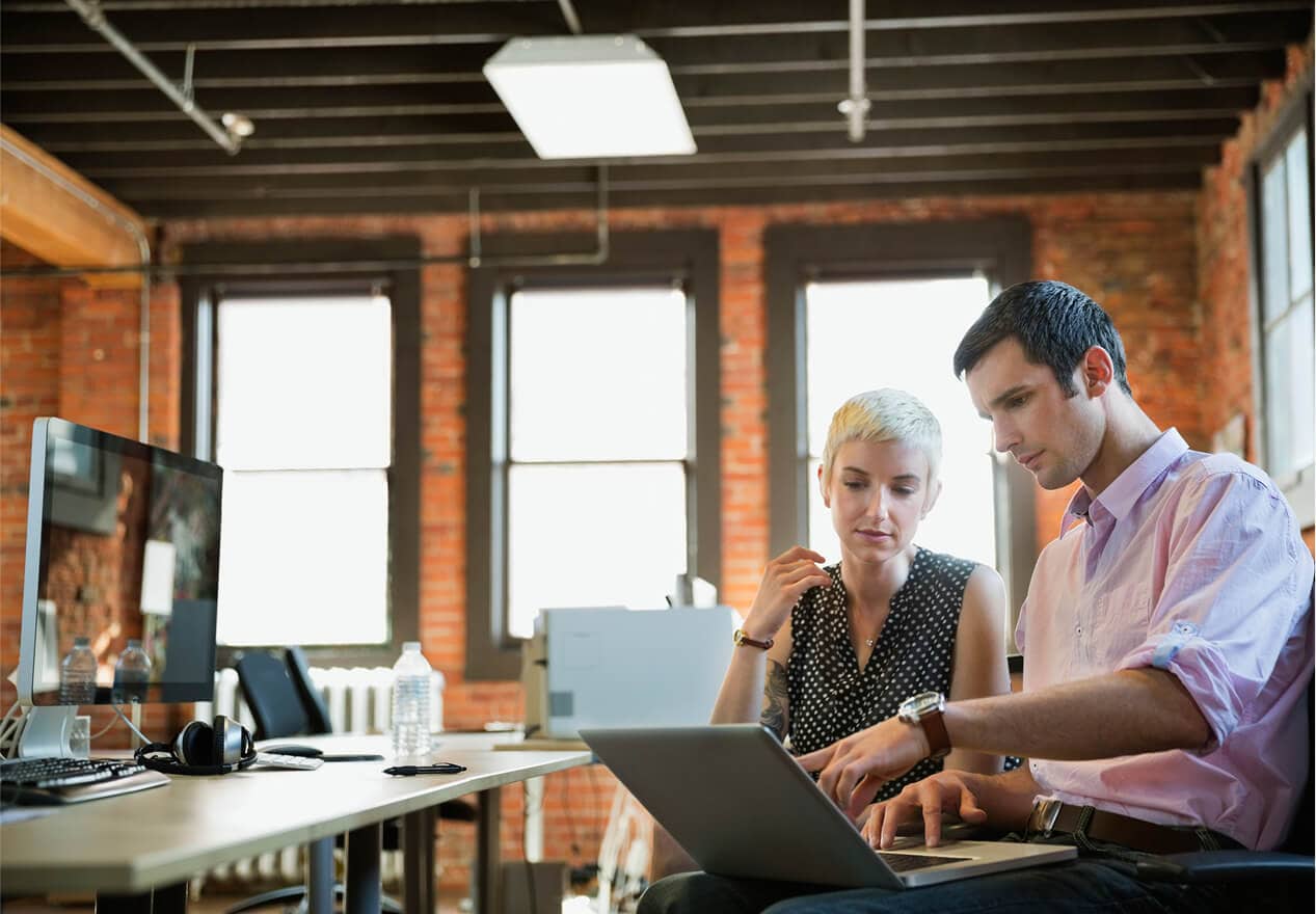 Two business owners in a modern office review information on a laptop, illustrating video business operations with ADT security. Two business owners in a modern office review information on a laptop, illustrating video business operations with ADT security.