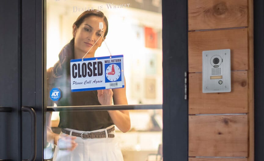 A flood sensor is mounted under a sink with visible plumbing, detecting leaks to help prevent damage. A business owner adjusts a “Closed” sign on a glass door, with an ADT sticker and intercom visible nearby.