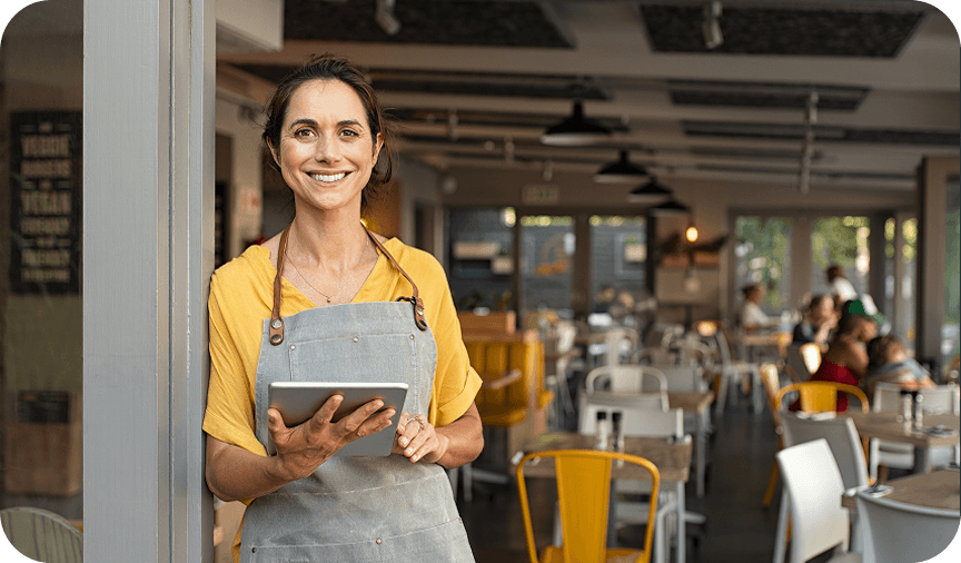 Café owner at restaurant entrance Smiling café owner in apron holding a tablet at the restaurant entrance.