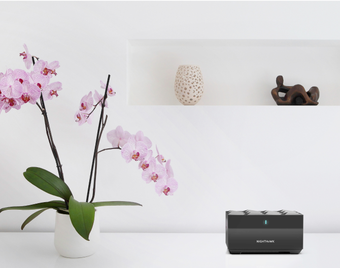 Netgear Mesh WiFi on a white table next to an orchid and vases Netgear Mesh WiFi on a white table next to an orchid and vases