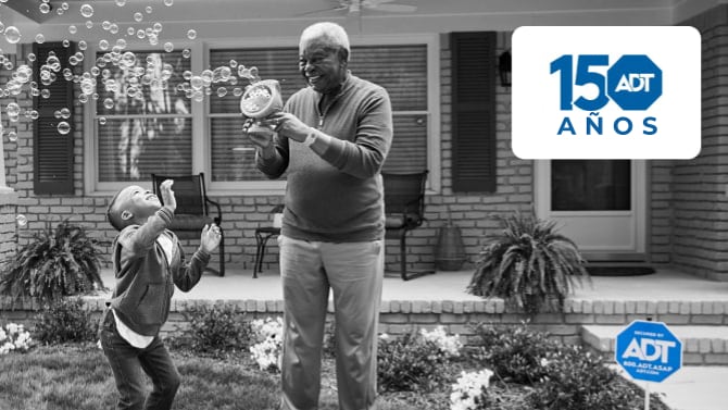 Un abuelo juega con sus nietos en su jardín con un letrero de ADT en el fondo.